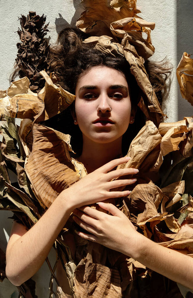 Portrait of young sexy brunette woman covered by leaves of dry, withered decorative banana tree, accuses the world for climate change - Φωτογραφία, εικόνα