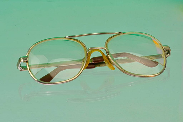 Reflectie van de bril. Gouden brillen, close-up. Een bril. Oude stijl brillen. Bril met transparante lenzen. Vintage Bril op gereflecteerde achtergrond. Sluiten van versleten brillen - Foto, afbeelding