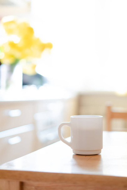 Taza de café blanco con servilleta en la mesa en el interior de la cocina real con luz solar natural brillante - Foto, imagen