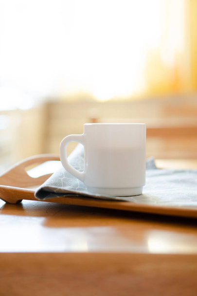 Tasse à café blanche avec serviette sur la table dans la vraie cuisine intérieure avec lumière naturelle du soleil - Photo, image