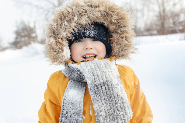 улыбающийся ребенок в меховом капюшоне в вязаном шарфе и оранжевой зимней куртке. на улице. модный ребенок. дети. крупным планом. зима - Фото, изображение