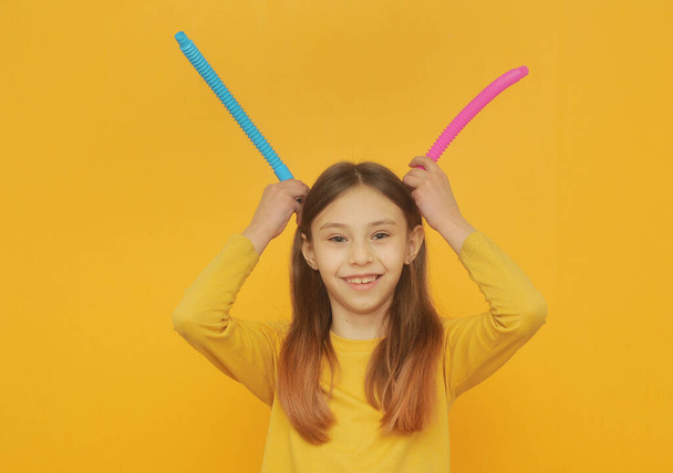 Kleines smartes Mädchen in gelben Klamotten spielt mit trendiger Spielzeug-Pop-Tube - Foto, Bild