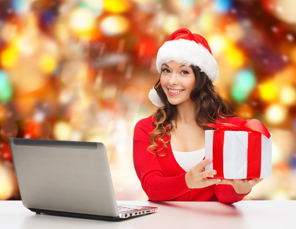 smiling woman in santa hat with gift and laptop - Fotó, kép
