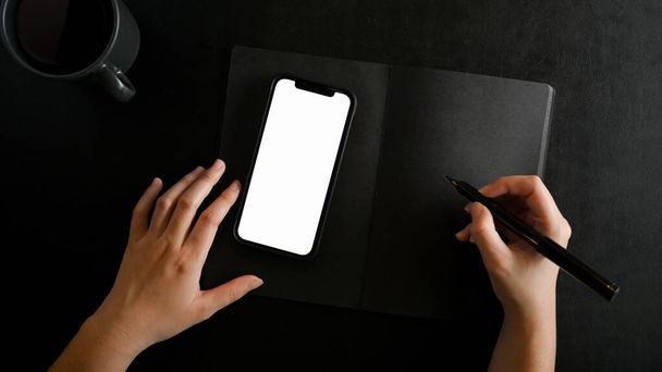 Top view, Vlakke lay, close-up vrouwelijke handen schrijven op zwart papier notitie in moderne zwarte werkruimte. - Foto, afbeelding