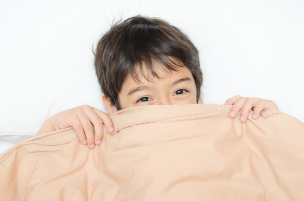 Menino deitado na cama com cobertura cobertor metade do rosto
 - Foto, Imagem