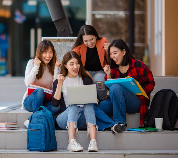 Group of Asian female students gathering at laptop and celebrating success with clenched fists, surprise and excited faces in university campus - Photo, Image