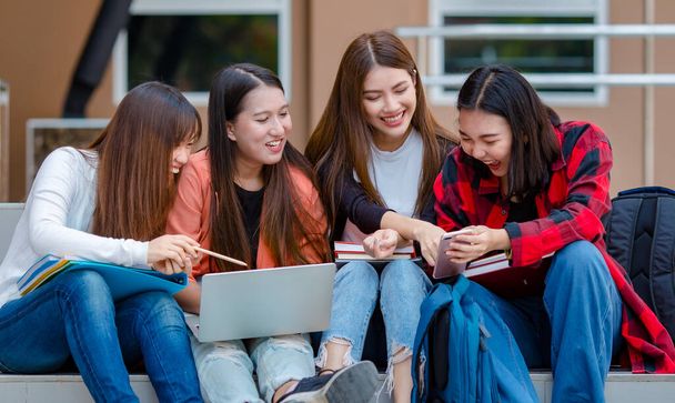 Gruppe asiatischer Studentinnen, die gemeinsam auf der Treppe sitzen und lustige Videos auf dem Smartphone ansehen, während sie auf dem Campus der Universität Pause machen. Intimer Begleiter des Lebenskonzepts von Teenagern. - Foto, Bild