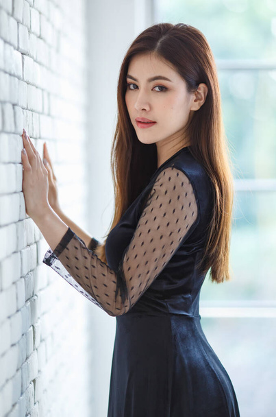 Portrait half lenght of cute content charming brunette Asian female, Lao ethnicity, in stylish black dress standing and pose with friendly positive and self confident pose. - Photo, Image