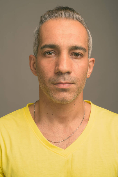 Studio πυροβόλησε όμορφος Περσικά άνδρα με γκρίζα μαλλιά που φοράει κίτρινο πουκάμισο γκρι φόντο - Φωτογραφία, εικόνα