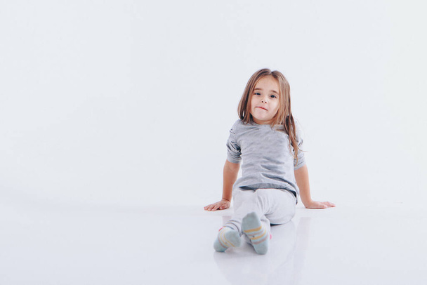 a little girl sits on the floor on a white background. Child promotes childrens clothes - Foto, Bild