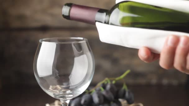 gieten van rode wijn in wijnglas op hout achtergrond - Video