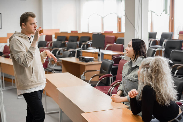Two girls and a guy are talking in sign language. Three deaf students chatting in a university classroom. - Фото, зображення