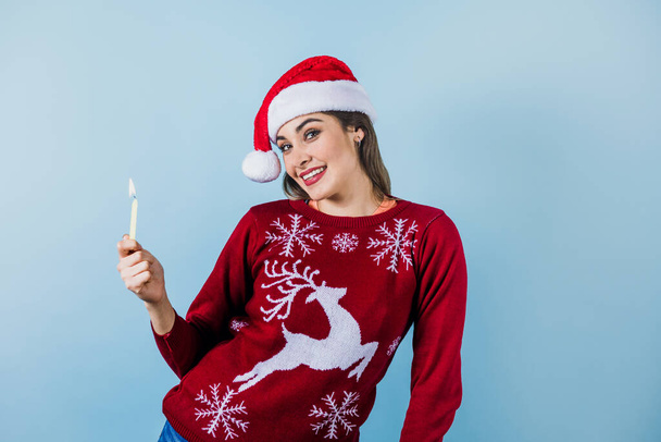 young latin woman holding christmas candle light in christmas hat on blue background in Mexico Latin America - Photo, Image