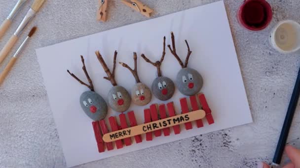 Making Diy Merry Christmas deer on greeting card postcard made of pebbles, sea stones, clothespins and branches on white background. Natural Eco style diy. Gift idea. Step by step. Top view. - Materiał filmowy, wideo