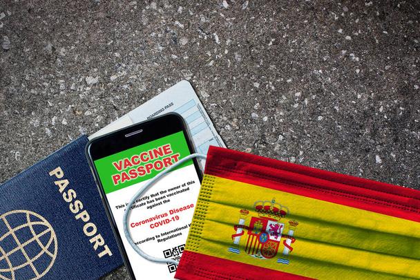 Spanje nieuwe normale reis met paspoort, digitaal vaccin op smartphone, instapkaart en gezichtsmasker met Spaanse vlag. Vaccin paspoort concept met kopieerruimte. - Foto, afbeelding