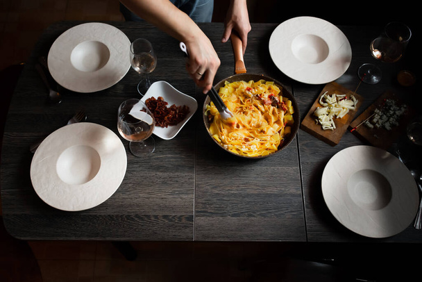 Man sets the table, homemade pasta, bacon, feta and tomatoes, cheeses with blue mold, wine. Deep plates for pasta. - 写真・画像