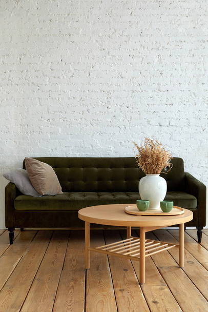Comfortable soft couch with cushions placed near round table decorate with vase with dried plants in lounge designed in loft style with brick wall and wooden floor - Fotoğraf, Görsel