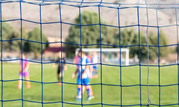 Football game in arena through soccer nets. Blurred players background - Foto, Bild