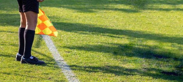 Fotbalový fotbalový rozhodčí asistent s vlajkou po ruce. Rozmazané zelené pole pozadí, zavřít - Fotografie, Obrázek