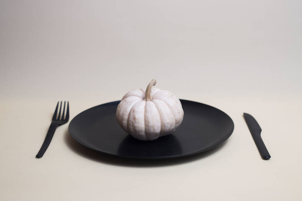 white pumpkin on black plate with black plastic knife and fork isolated on light background. Image contains copy space - Zdjęcie, obraz