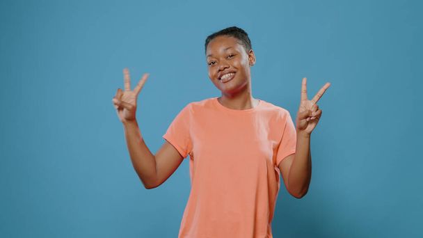 Fröhliche Frau macht Friedenssymbol mit Fingern und lächelt - Foto, Bild