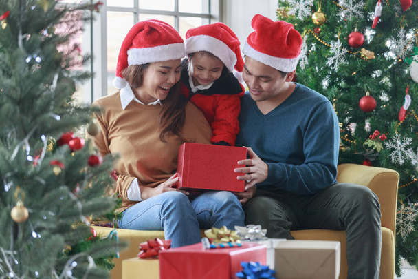 Aasialainen onnellinen perhe ja pieni tyttö avoin magic lahjapaketti joulukuusi olohuoneessa, joka on sisustettu joulun festivaali. Joulupukin hatut istuvat sohvalla. Käsitteen joululahja laatikko - Valokuva, kuva
