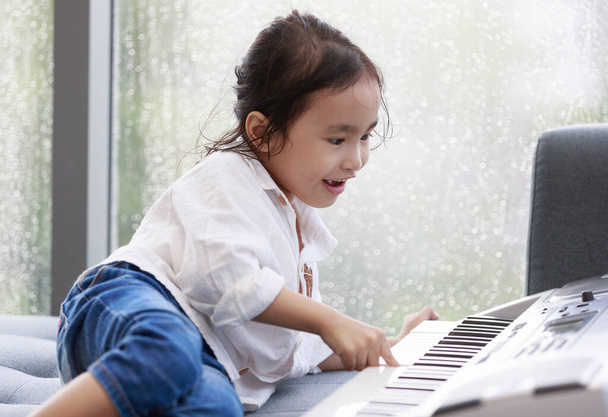 Asiatica ragazza felice sta suonando il pianoforte in una sala prove di musica, l'atmosfera fuori sta piovendo. Gocce d'acqua sul bicchiere. Concetto bella educazione all'apprendimento - Foto, immagini