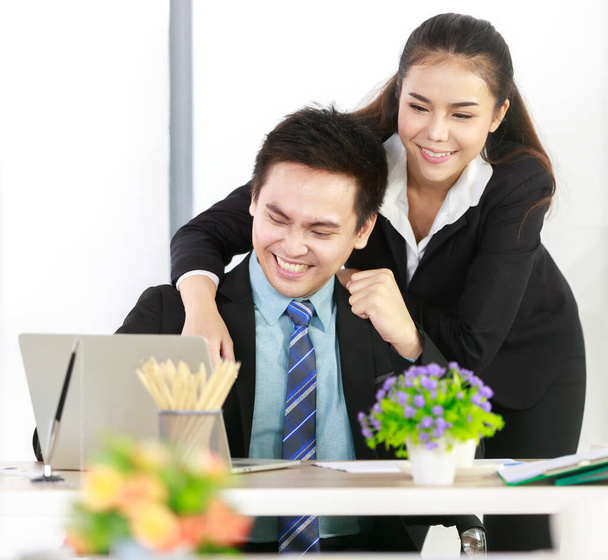 Азиатский бизнесмен и бизнесвумен в черных костюмах работают вместе в ноутбуке в офисе, показывая радость, когда работа была успешной. Успех концепции счастливая веселая работа - Фото, изображение