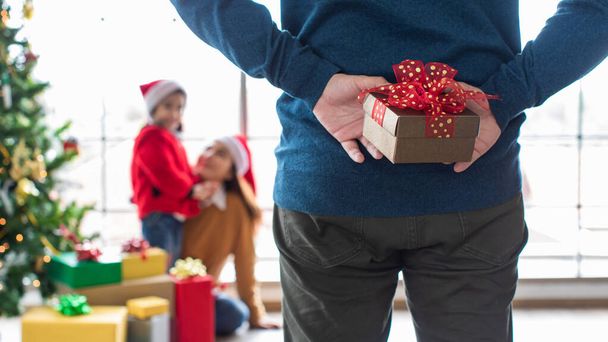 Focus to gift box on asian father hand who holding gift box hidden on backward for surprise with his daughter in Christmas Happy New festival which celebrate during December to January. - Foto, immagini