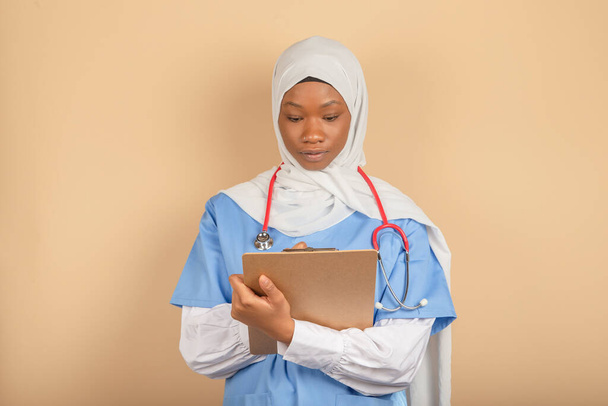 Nuori nainen muslimien uskonnon valkoinen huntu pitämällä leikepöydälle ja kirjallisesti jotain lähikuva. Sairaanhoito, vakuutus, resepti. - Valokuva, kuva