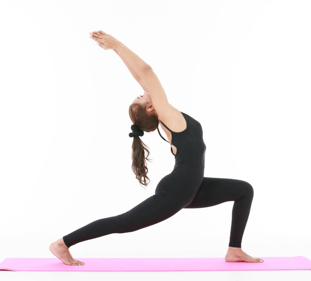 Vista lateral de la hembra asiática haciendo pose Crescent Lunge con los brazos levantados mientras practica yoga sobre fondo blanco - Foto, imagen