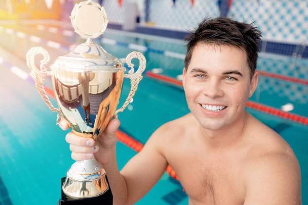 Young man winner in swim pool with champion gold trophy with sun light - Foto, Bild