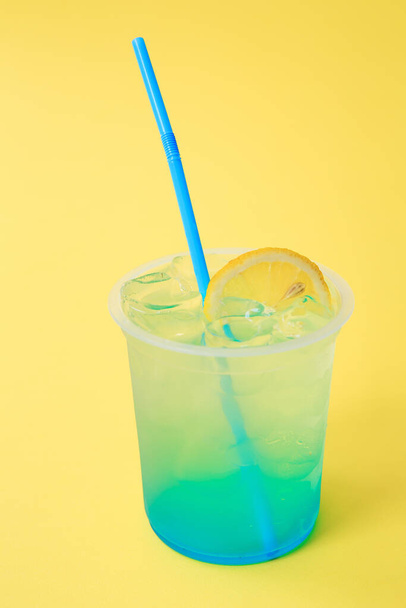 レモンとレモネードブルーラグーン、冷たいさわやかな飲み物や黄色の背景に氷と飲み物を持つガラス - 写真・画像