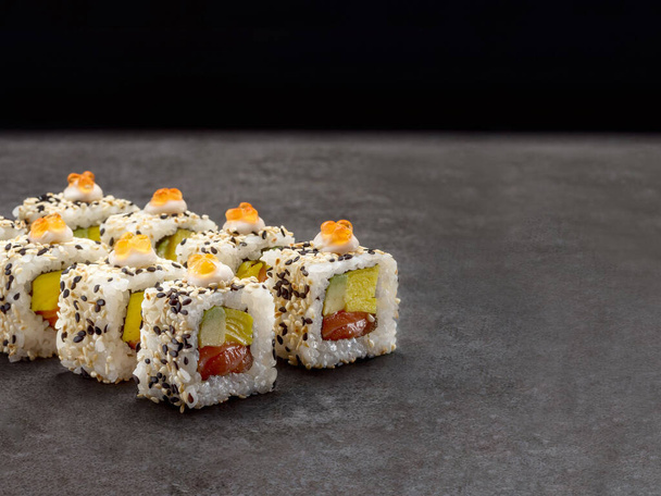 Σολομός, αβοκάντο, ομελέτα με αυγό τυλιγμένη σε ρύζι. Σερβίρεται με χαβιάρι κόκκινου σολομού και σουσάμι. Ιαπωνικό παραδοσιακό πιάτο ρολό σούσι σε μπετόν φόντο. Μονό αντικείμενο. Αντιγραφή εικόνας χώρου - Φωτογραφία, εικόνα