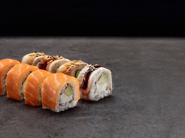 Rollo de sushi japonés con aguacate y queso crema dentro del rollo. Plato asiático con salmón y anguila encima sobre fondo de hormigón oscuro. Copia la imagen espacial. Objeto único. De adentro hacia afuera sushi - Foto, imagen