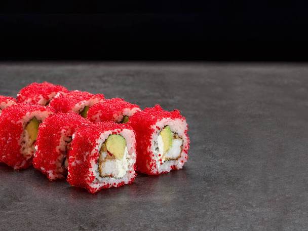 Crunchy black tiger shrimp inside Japanese sushi roll with avocado and cream cheese inside. Red flying fish roe Tobiko on top. Masago caviar Asian roll. Inside out sushi. Concrete background. - Photo, Image