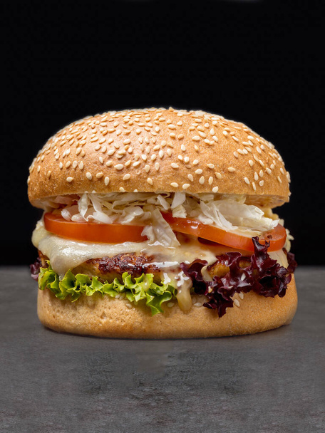 Juicy burger with grilled chicken cutlet, melted Mozzarella cheese, tomato slices, lettuce, Chinese cabbage, creamy sauce in wheat bun with sesame seeds served without plate, dark concrete background - Foto, immagini