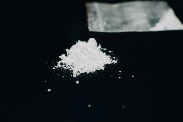 Polvo de drogas de cocaína en bolsa de plástico y pila de polvo de cocaína sobre fondo negro.. - Foto, Imagen