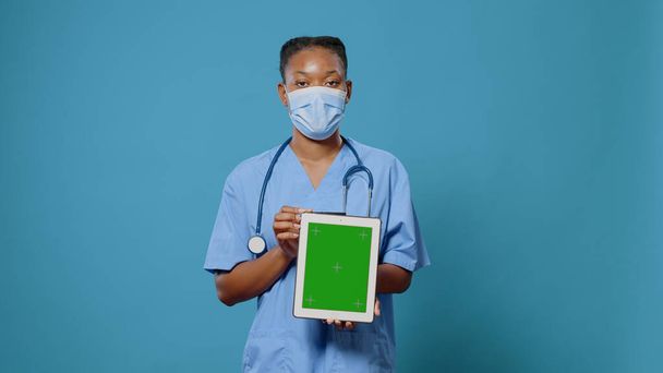 Vrouw verpleegster toont tablet met groen scherm naar camera - Foto, afbeelding