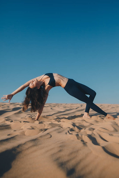 Fiatal gyönyörű barna nő fekete ruhában pózol a homokos tengerparton. Vonzó nő boldogan táncol, pózol ellen kék ég háttér - Fotó, kép