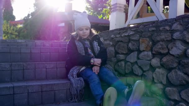 Piękne dziecko dziewczyna kopie z nogi siedzi na schodach - Materiał filmowy, wideo
