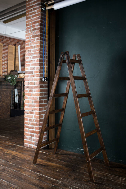 Wooden brown ladder stepladder on a wooden floor near a dark blue wall for installation work - Photo, Image