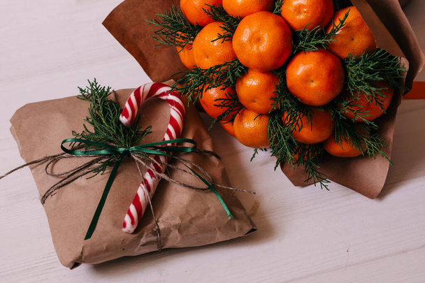 Gifts wrapped in craft paper decorated with spruce branches and tangerines bouquet - Photo, Image