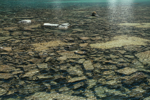 Prachtige achtergrond van stenige bodem in transparant water van gletsjermeer in zonlicht. Zonnig decor met veel stenen in helder water van gletsjermeer. Textuur van het bergmeer met gereflecteerd licht. - Foto, afbeelding