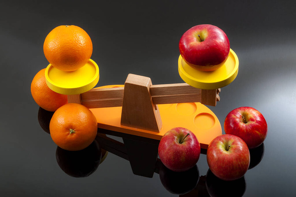 Tento idiom, porovnávající jablka a pomeranče, odkazuje na rozdíly mezi nesrovnatelnými nebo nesouměřitelnými položkami. Tento koncept ilustrují 2 skupiny jablek a pomerančů v rovnovážném měřítku - Fotografie, Obrázek