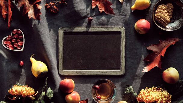 Blackboard, frame and Autumn decor. Chrysanthemum flowers, bunny tail grass and red oak leaves, pumpkins, cranberry. Autumn decorations, top view. Flat lay on dark textile with copy-space, text place. - Photo, image