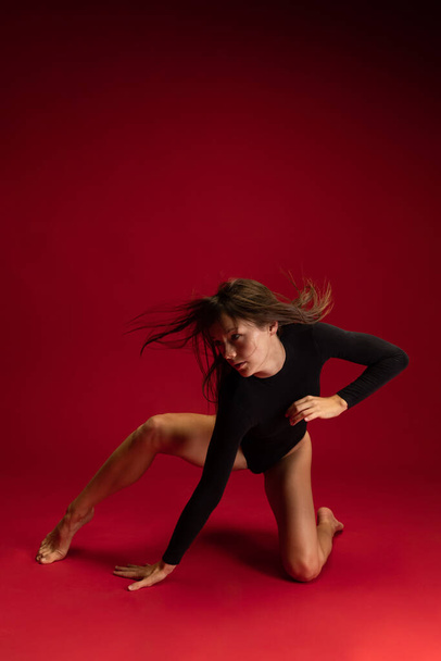 Portrait of emotional young flexible contemp dancer, ballerina dancing isolated on dark red background. Art, beauty, inspiration concept. - Fotoğraf, Görsel