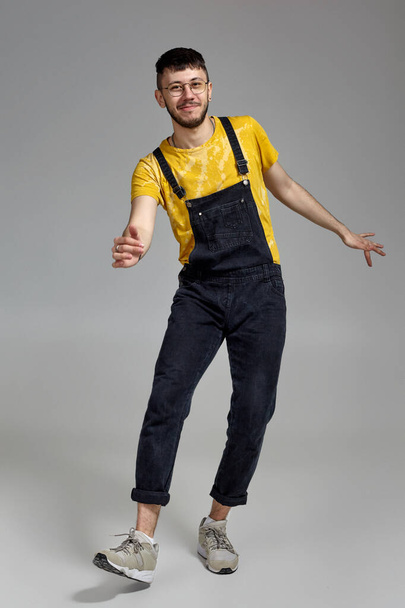 Full-length portrait of a funny guy dancing in studio on a gray background. - Photo, Image