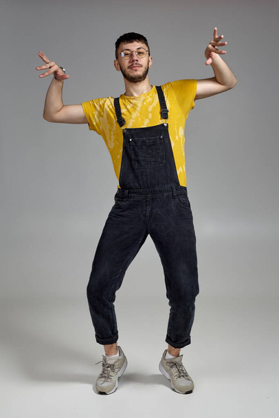 Full-length portrait of a funny guy dancing in studio on a gray background. - Foto, afbeelding