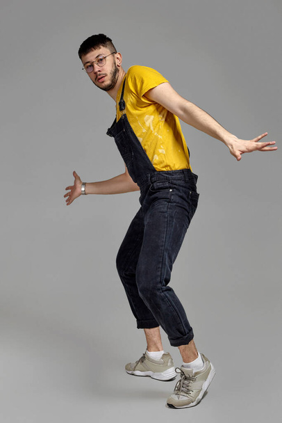 Full-length portrait of a funny guy dancing in studio on a gray background. - Photo, image